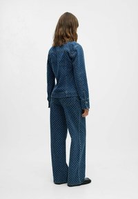 Conjunto de chaqueta de mezclilla y pantalones de pierna ancha en azul oscuro con un patrón floral blanco, con cierres de botón y detalles cosidos.