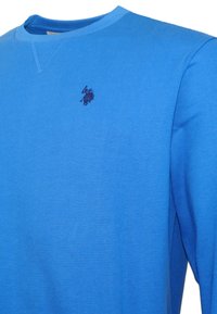 Modrá polovičná košeľa s dlhými rukávmi a okrúhlym výstrihom, na ľavej hrudi je malé tmavomodré vyšívané logo polo hráča.