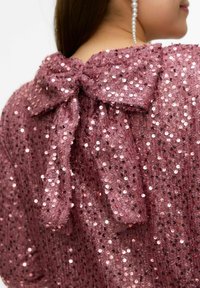 Pink palietkjole med stor sløjfe på ryggen, der har en tekstureret overflade og glitrende palietter. Stoffet er gennemsigtigt med et blødt, flydende udseende.