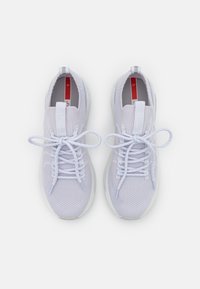 Hellgraue Sportschuhe mit einem Obermaterial aus Mesh, flachen Schnürsenkeln und einem gepolsterten Schaft. Die Sohle ist weiß und hat eine leichte Erhöhung an der Ferse.