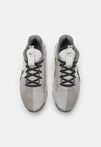 Buty sportowe Nike z szarą siateczkową cholewką, czarnymi sznurowadłami, teksturowanym wzorem w kratkę oraz białym logo. Minimalistyczny design o opływowym kształcie.