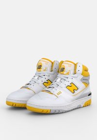 Scarpe da ginnastica alte bianche con accenti gialli, con una tomaia in pelle texturizzata, dettagli traforati e supporto per la caviglia imbottito.