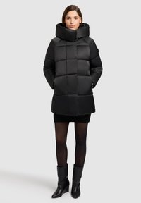 Geacă neagră matlasată cu guler înalt, pliabil și model matlasat. Dispune de buzunare laterale și croială lejeră, purtată peste o fustă neagră.