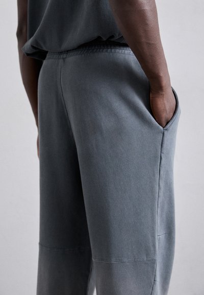Pantaloni de trening gri din bumbac cu o croială lejeră, dotati cu buzunare laterale și cusături vizibile. Textură moale și detalii cu talie elastică.