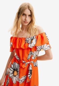 Schoudervrije oranje jurk met een gerimpelde halslijn, versierd met grote zwart-witte bloemenpatronen en een gestrikt taille-detail.