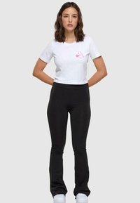 Witte cropped t-shirt met roze Minnie Mouse graphic, gecombineerd met zwarte strakke broek en witte sneakers, afgebeeld tegen een neutrale achtergrond.