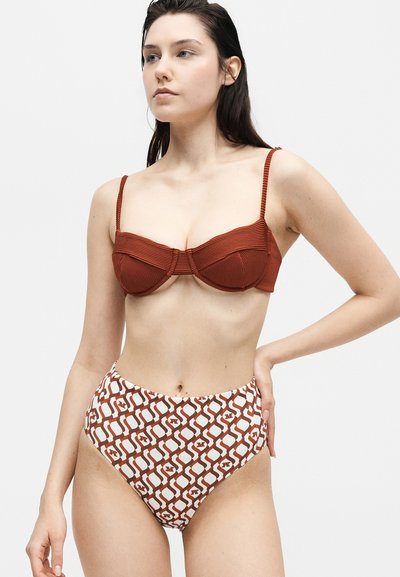 Νέα γυναίκα φοράει ριμπ μπικίνι τοπ σε σκουριά χρώμα και μπικίνι στρόγγυλο καπιτονέ με μοτίβο που συνδέει καφέ και λευκό σχέδιο.