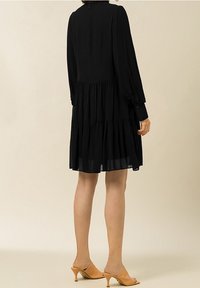 Musta pitkähihainen mekko, jossa on kerrostettuja röyhelöitä ja korkea kaulus. Sujuva kangas, nilkkapituiset. Yhdistetty vaaleanruskeisiin muloihin.