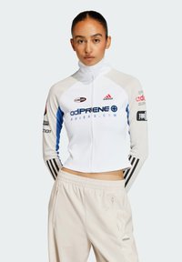 Vit zip-up idrottsjacka med blå accenter och svarta ränder, med logotyper och varumärkesinformation. Bar med ljusbeiga, löst sittande byxor.