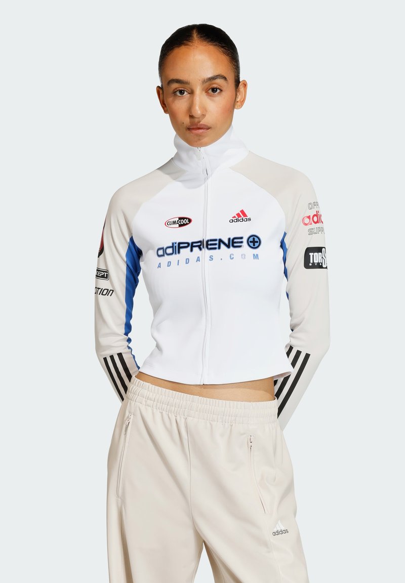 Hvid zip-up træningsjakke med blå accenter og sorte striber, der har logos og branding. Bæres med lysebeige, løs pasform bukser.