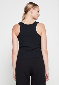 T-shirt noir à rayures côtelées avec une silhouette ajustée et des bretelles larges, présentant un col rond et une longueur crop. Texture lisse.