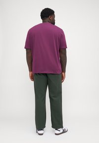 Kortermet, maroon t-skjorte med rund hals, kombinert med grønne bukser og hvite sneakers med svarte striper og en teksturert såle.