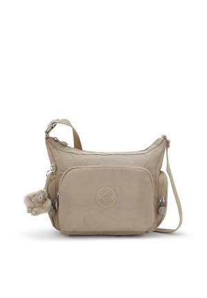 Beige crossbodytas gemaakt van zacht materiaal met een afgeronde vorm. Voorzien van een voorvak, ritssluiting en een zacht aapje als sleutelhangeraccessoire.