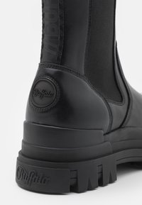 Botín negro de cuero con paneles laterales elásticos, suela de goma texturizada y un ligero tacón. Cuenta con un logotipo circular de "Buffalo" en el tacón.