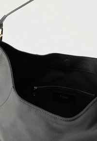 Sac en cuir gris avec un extérieur texturé, ouverture par le dessus et une poche intérieure zippée. Doté d'une doublure noire lisse et d'une fermeture éclair dorée.