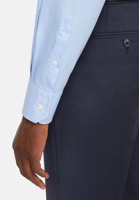 Jasnoniebieska koszula z długim rękawem z guzikami przy mankietach, w połączeniu z ciemnogranatowymi, teksturowanymi spodniami. Koszula ma białe guziki i dopasowany krój.