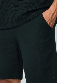 Shorts noirs en tissu texturé, dotés de poches latérales et d'une coupe décontractée. La taille est élastique pour un confort optimal.