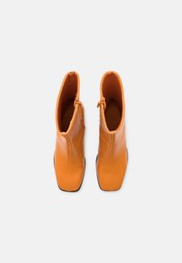 Botas de tobillo de cuero naranja con un diseño elegante, punta cuadrada y cremalleras laterales. Textura suave y suelas de goma negra.