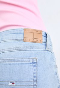 Ljust blå denimjeans med en läderetikett i midjan där "TOMMY JEANS" är präglat, samt en liten tri-färgad logotyp på bakfickan.