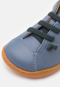 Scarpa di pelle blu con lacci verdi, punta rotonda, suola in gomma arancione e cuciture visibili. Dettagli della superficie testurizzata notati.