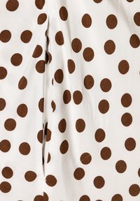 Tissu blanc recouvert de pois marron ; présente des plis pour le détail de design. Texture lisse avec des motifs circulaires distincts.