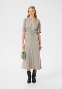 Light gray dress with short puff sleeves, zipper front, and gathered waist; paired with a small, two-tone handbag and black knee-high boots.