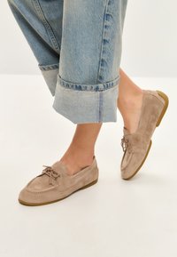 Beige ruskinds loafers med rund tå, snøre detaljer og gummisål. Båret med opkrøllede lyseblå jeans.