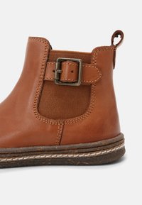 Bottine en cuir marron avec panneau élastique latéral, bride décorative avec boucle, languette de tirage et semelle en caoutchouc cousue.