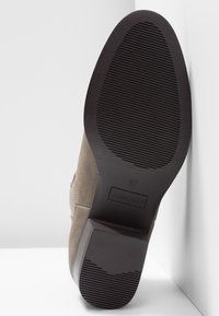 Semelle de bottine en daim taupe avec semelle en caoutchouc noire, taille 37, avec le nom de marque "ANNA FIELD" visible sur le talon.