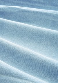 Tela de denim azul claro con un patrón de tejido diagonal visible y una textura suave, dispuesta en pliegues suaves y fluidos.