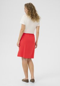 Red elastic-waist skirt with a smooth texture, knee-length, paired with a short-sleeve white top. Simple design, suitable for casual wear.