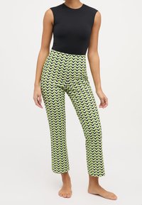 Svart ärmlös topp matchad med gröna och svarta byxor med zickzackmönster. Byxorna har en slim fit-design och är cropped i längden.