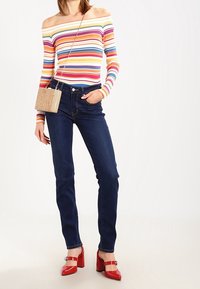 Randig off-shoulder topp, mörkblå skinny jeans och röda klackskor. Handväskan är beige med en texturerad yta.