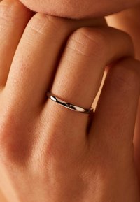 Dunne zilveren ring op een vingertop, met een gladde gepolijste oppervlakte en een eenvoudig, rond ontwerp zonder versieringen.