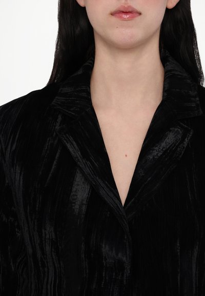 Schwarzer Samt-Blazer mit weichem, strukturiertem Finish. Verfügt über breite Revers und einen tiefen V-Ausschnitt, der eine elegante Silhouette schafft.