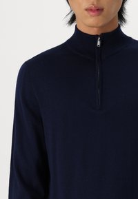 Suéter azul marino con cremallera en el cuello, fabricado en material suave, con un alto cuello y hombros sin costuras para un diseño limpio.