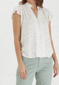 Weißes Blumenhemd mit gerafften Kappenärmeln, versehen mit kleinen gelben und rosa Blumenmustern, kragenlosem Ausschnitt und durchgeknöpftem Vorderteil.