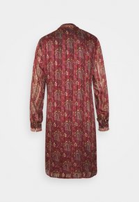 Pitkähihainen mekko syvän burgundin värisessä kankaassa, jossa on monimutkaisia paisleyn kuvioita kullassa ja kermaisen valkoisessa, varustettuna ryppyreunuksilla ja rennolla siluetilla.