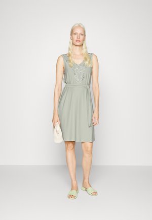 Vestido verde sem mangas com bordados de renda no decote, cintura cingida e um design simples. Combinado com sandálias verde-claro e uma clutch.