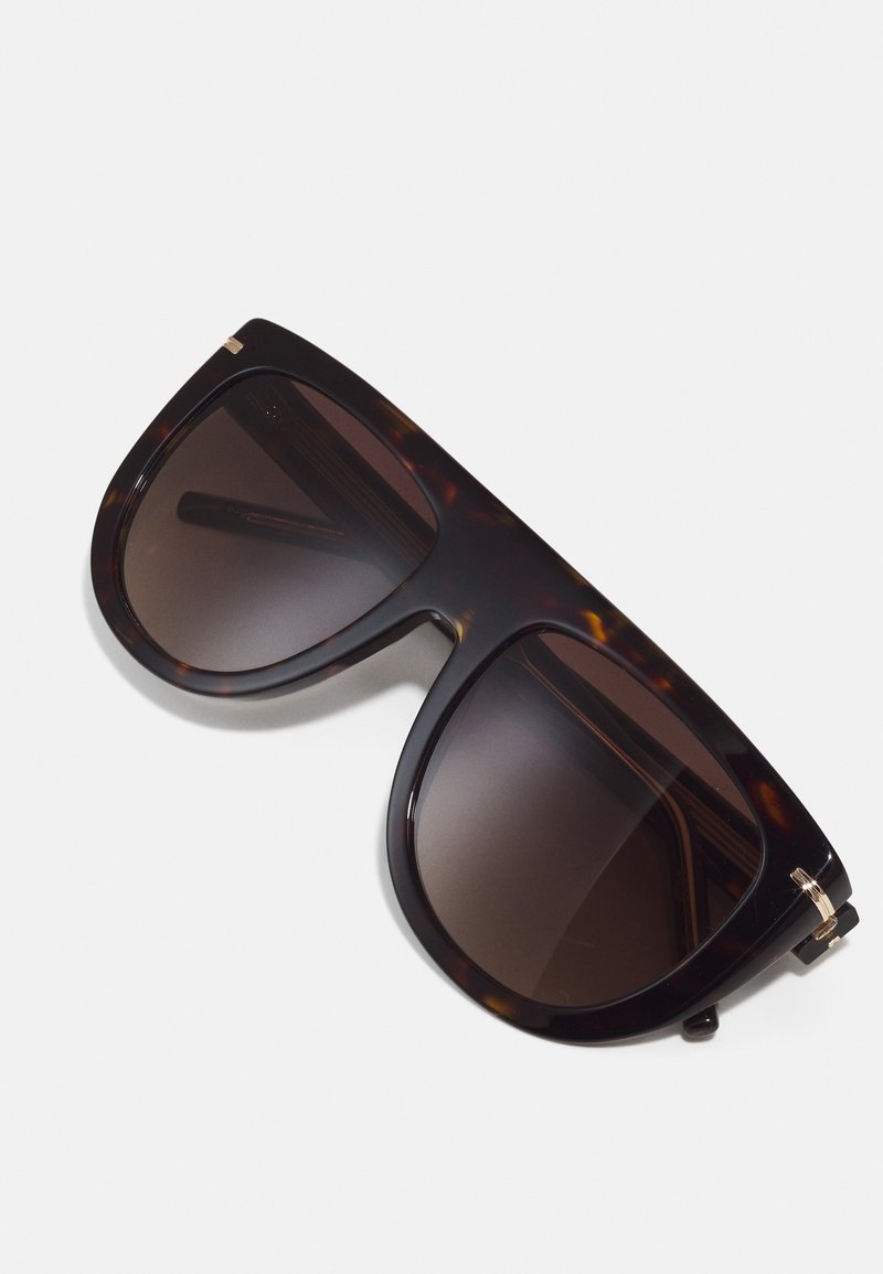 Schildpad-sunglasses mit übergroßen dunklen Gläsern. Glatter Kunststoffrahmen mit goldfarbenen Akzenten an den Schläfen. Winkeliges Design.