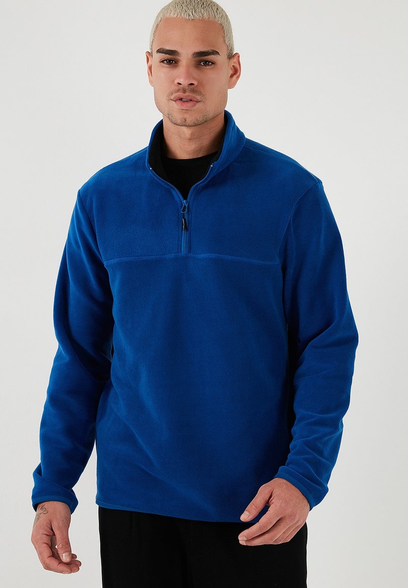 Blauer Fleece-Pullover mit einem Viertel-Reißverschluss auf der Vorderseite, langen Ärmeln und glatter Textur. Verfügt über ein kontrastierendes Panel über der Brust.