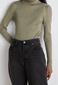 Ribbed, oliwkowy golf z bufiastymi akcentami na ramionach, zestawiony z wysokimi, ciemnoszarymi dżinsami z guzikami i kieszeniami.