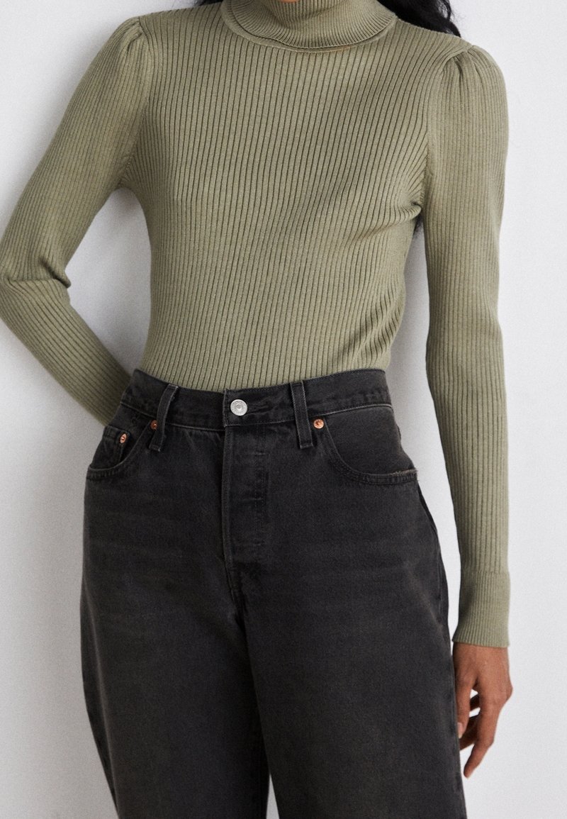 Ribbed, oliwkowy golf z bufiastymi akcentami na ramionach, zestawiony z wysokimi, ciemnoszarymi dżinsami z guzikami i kieszeniami.