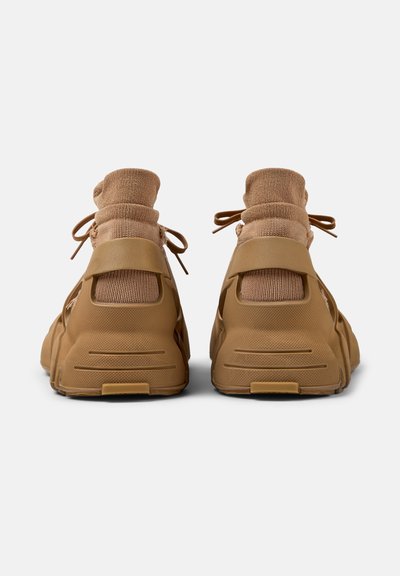 Paar beige High-Top-Sneaker mit gestrickten Knöchelabschlüssen und dicken Gummisohlen, von hinten auf weißem Hintergrund gesehen.