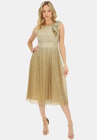 Złota sukienka z dopasowanym gorsetem, plisowanym dołem i falbaniastym akcentem na jednym ramieniu. Wykonana z błyszczącej, teksturowanej tkaniny.