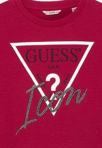 Maglione in cotone rosso con logo stampato triangolare con "GUESS" e "Icon" in nero, impreziosito da strass.
