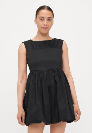 Svart ärmlös klänning med en figurnära bodice och ett draperat kjoldel. Tillverkad av lättviktigt tyg, har rund halsringning och en minimalistisk design.