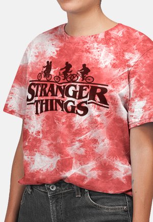 Rode tie-dye T-shirt met korte mouwen, voorzien van een zwarte graphic van drie figuren op fietsen en de tekst "STRANGER THINGS" eronder. Katoenen materiaal.