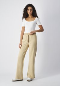 Pantaloni beige a gamba larga con vita elastica e coulisse, abbinati a una maglietta aderente bianca a maniche corte e sneakers bianche.