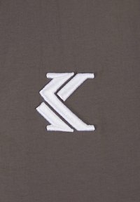 Grått stoff har et fremtredende hvitt brodert logo som viser kantete former og rene linjer, noe som forbedrer det generelle designet.